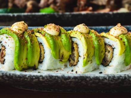 A colorful four-piece sushi roll is topped with a mayo sauce and bright green avocados.