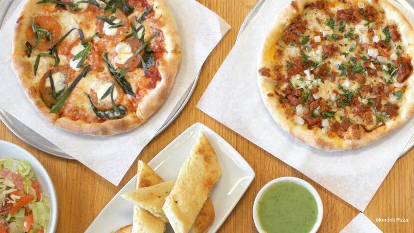 Two pizzas and breadsticks that are filled with veggies and dipping sauce