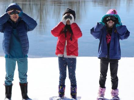 Three kids holding binoculars explore Aurora's wintery backdrop.