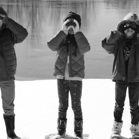 Three kids holding binoculars explore Aurora's wintery backdrop.