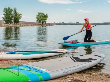 A young woman approaches the sandy beach at Cherry Creek State Park with her paddleboard