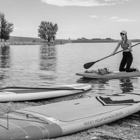 A young woman approaches the sandy beach at Cherry Creek State Park with her paddleboard