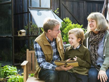 Grandparents and grandchild read a book outside.